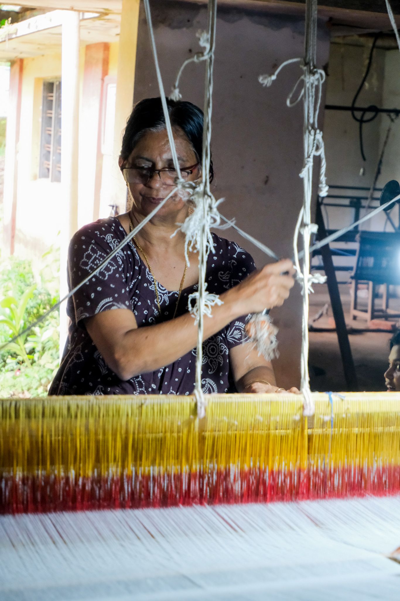 A weaver smiling as she works the threads at her loom