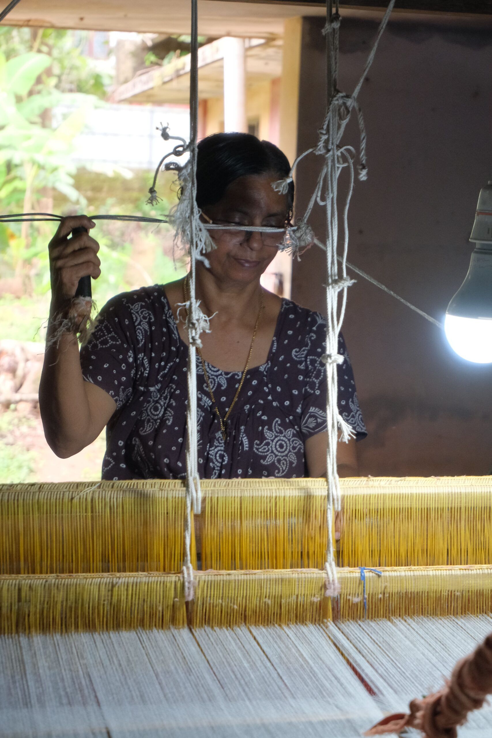 A weaver drawing threads at the loom, the golden warp in front of her