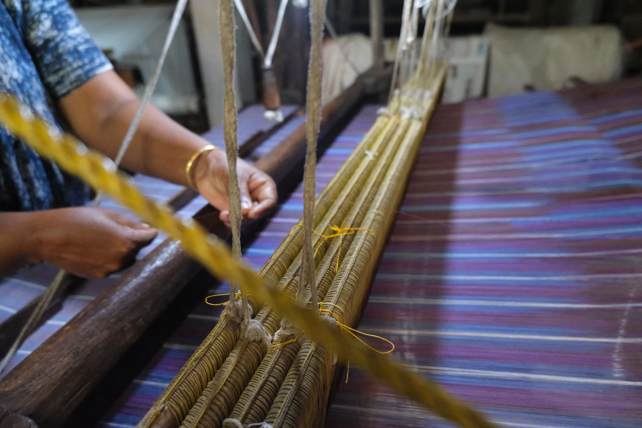 Hands passing the weft through the warp on the loom
