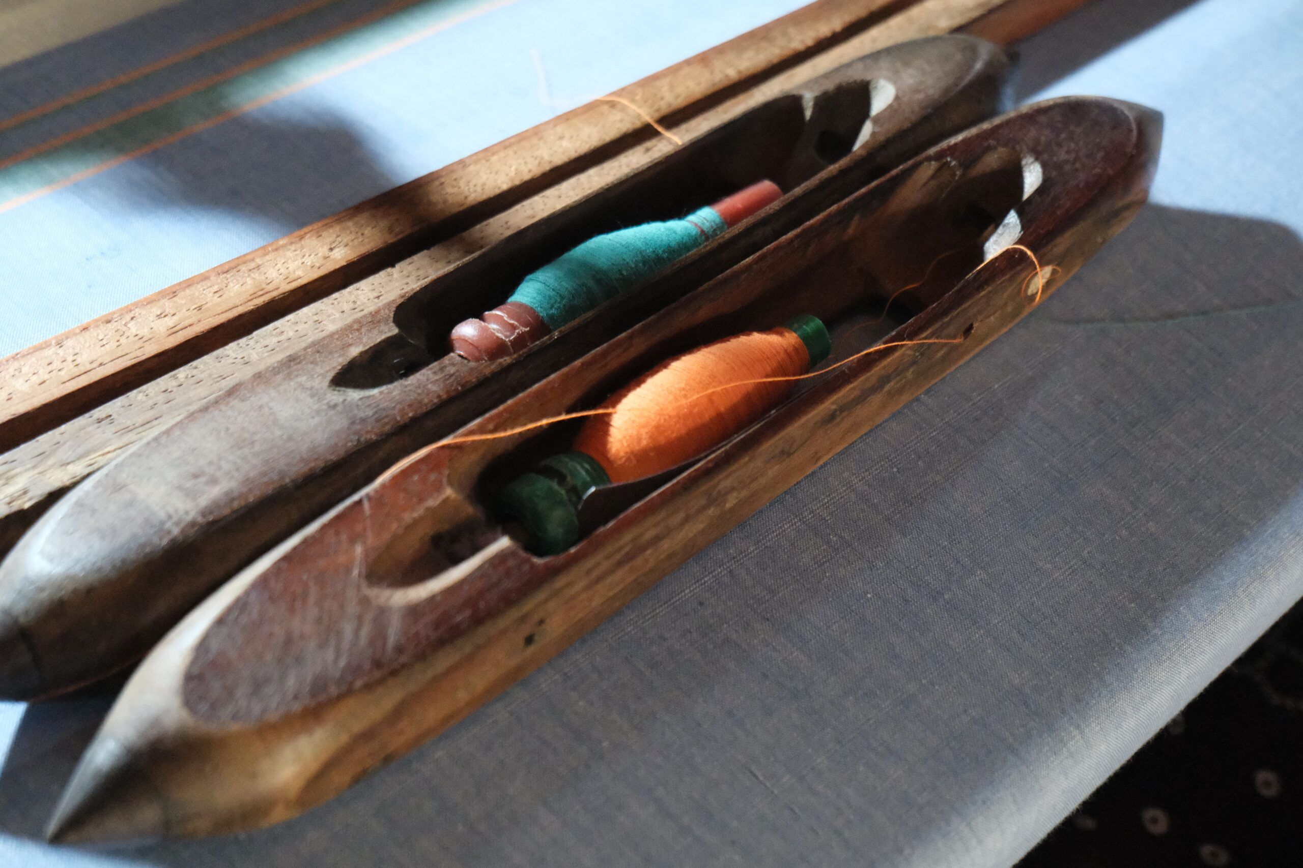 Two wooden shuttles, each holding a bobbin of thread