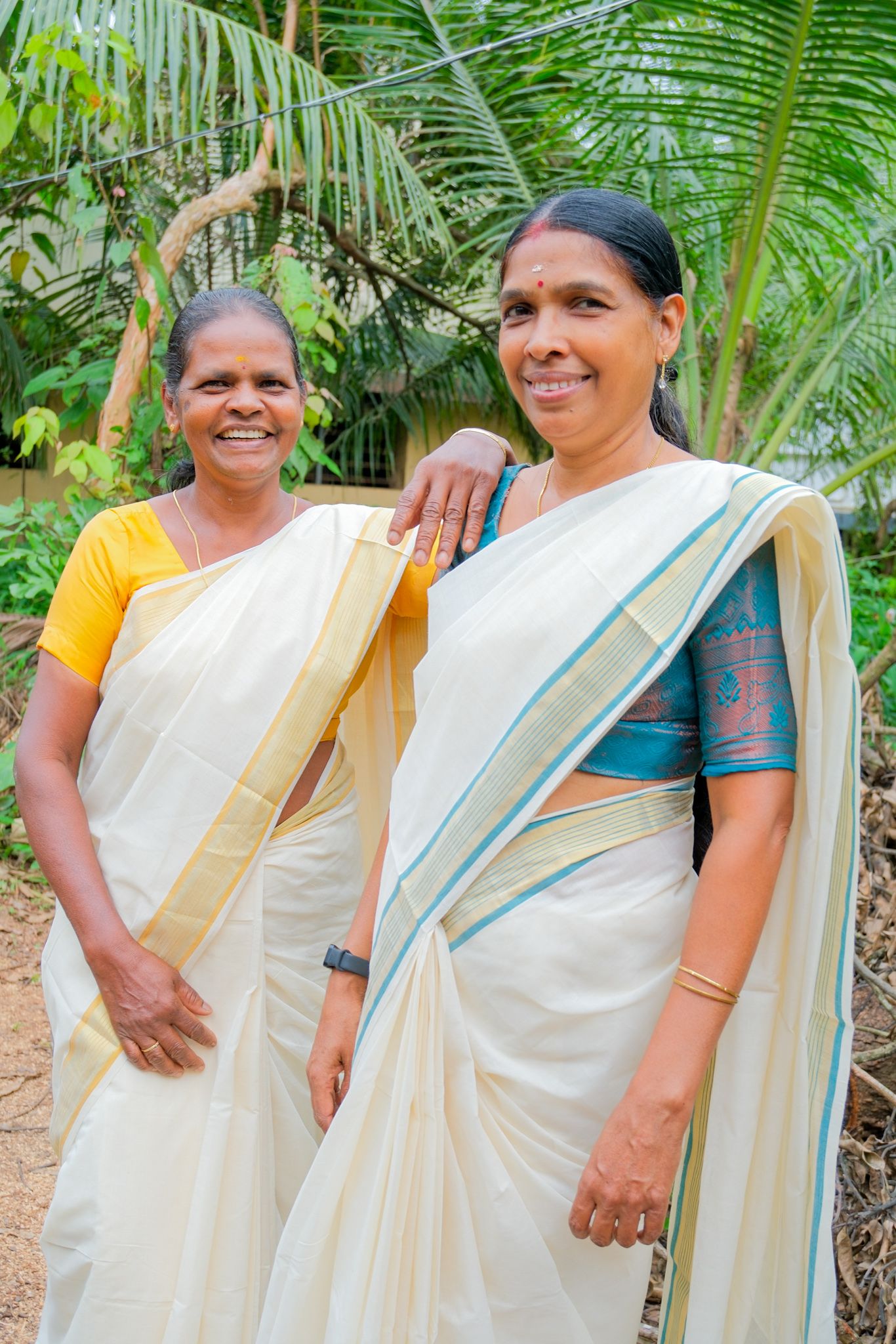 Two weavers of Chengamanad smiling in their Kasavu sarees among coconut palms