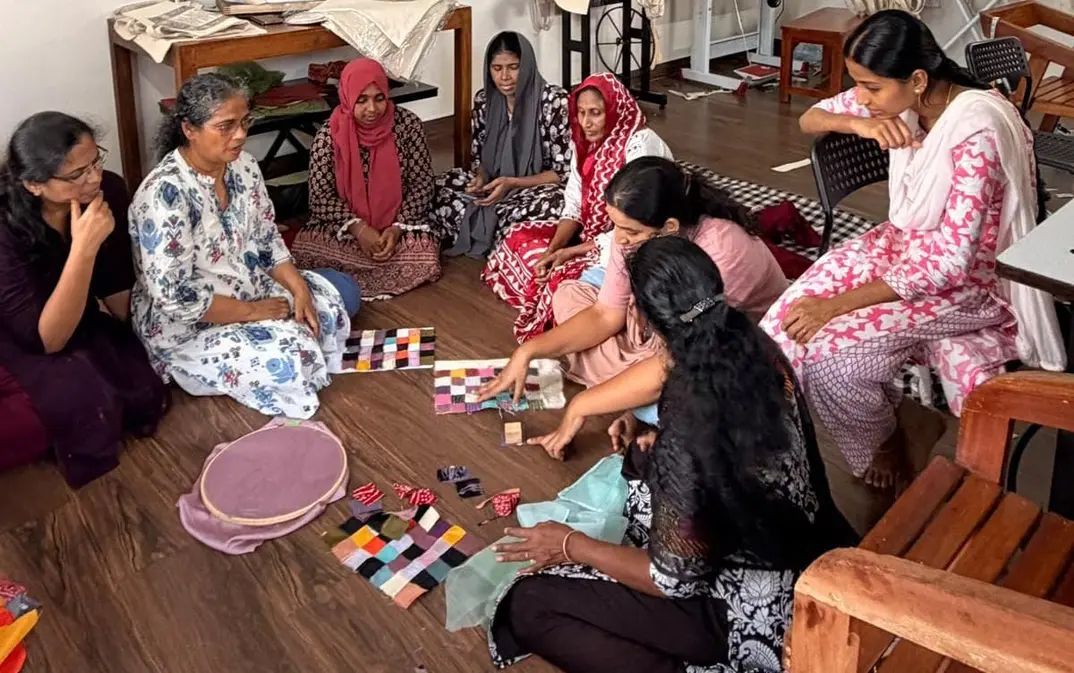 Women from different communities sitting in a circle on the floor, planning a patchwork layout together