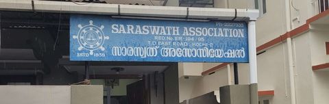 A blue signboard reading ‘Saraswath Association, T.D. East Road, Kochi-2, Estd. 1938’ mounted on a building’s covered entrance.