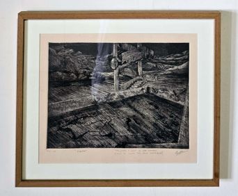 A framed black-and-white print, signed in pencil below the image, showing a dark hollow of collapsed beams and rubble with a shaft of light falling through.