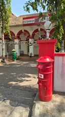 Red and green pillar postboxes outside an arched building with India Post signage