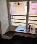 Window-side seating nook with a curved built-in bench and a small table holding a closed laptop.