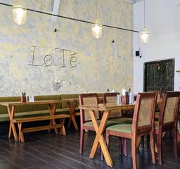 Cafe interior with a wire ‘Le Té’ sign on a weathered wall, wooden tables and cane chairs.
