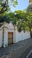 Whitewashed wall with an ornate wooden gate, trees overhead