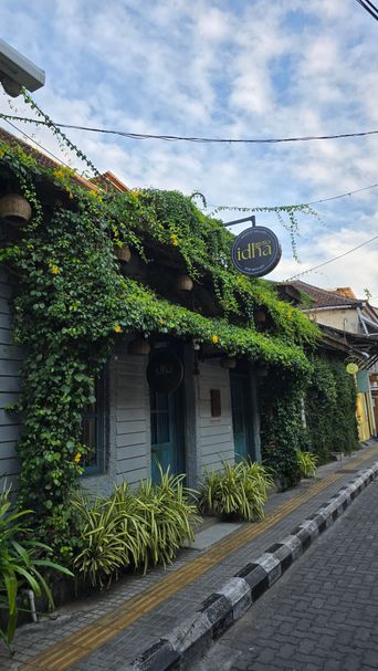 Vine-covered shopfront with a round sign reading ‘idha’