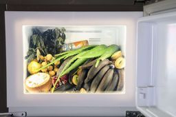 Open refrigerator lit from inside, packed with jackfruit, bananas, longan, pomegranate and long aloe vera leaves, part of a Biennale installation at Aspinwall House.
