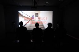 Visitors sit in silhouette watching a video projection titled ‘Killing Fields of Celluloid’ showing a staircase inside a building, at SMS Hall.