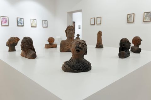 Terracotta bust sculptures of faces and figures arranged on a white plinth at SMS Hall, framed drawings on the walls behind.