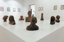 Terracotta bust sculptures of faces and figures arranged on a white plinth at SMS Hall, framed drawings on the walls behind.