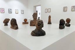 Terracotta bust sculptures of faces and figures arranged on a white plinth at SMS Hall, framed drawings on the walls behind.
