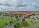 An aerial view of Cochin International Airport’s red-roofed terminal building, with a large car park, access roads and green lawns in the foreground under a partly cloudy sky.