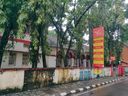 The cream-and-red Fort Kochi Post Office building seen from the street through overhanging trees, with a red-and-yellow India Post signboard listing services out front.