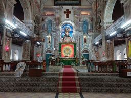 The ornately painted interior of Santa Cruz Basilica, showing a gold-domed altar and a red-carpeted aisle leading up marble steps between decorated pillars.