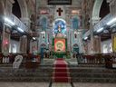 The ornately painted interior of Santa Cruz Basilica, showing a gold-domed altar and a red-carpeted aisle leading up marble steps between decorated pillars.