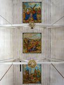 Three framed Stations of the Cross paintings mounted in a row along a white wooden vaulted ceiling.