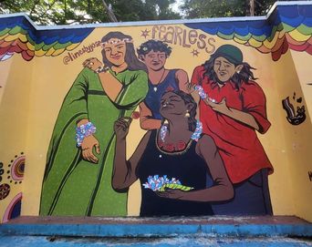 A wall mural on Poovath Street titled 'Fearless', showing four women adorned with flowers and bangles under a rainbow-scalloped border.