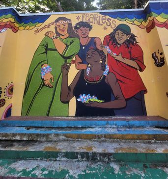 A wall mural on Poovath Street titled ‘Fearless’, showing four women adorned with flowers and bangles under a rainbow-scalloped border.