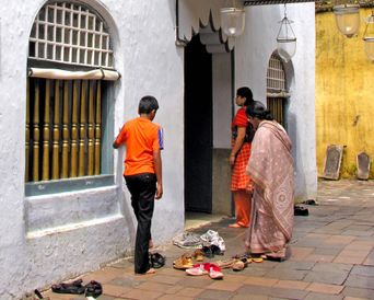Two women and a boy stand outside the synagogue’s arched entrance, sandals left in rows on the ground before going in.