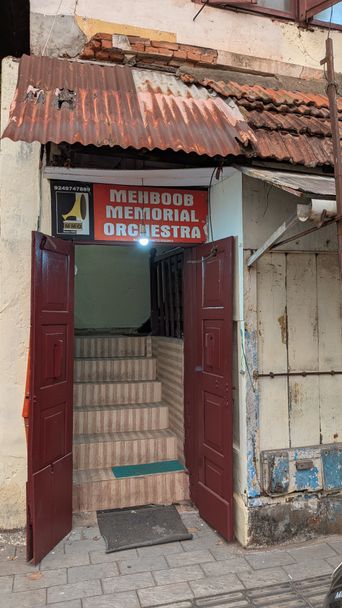 Old doorway and staircase with red double doors, sign reading ‘Mehboob Memorial Orchestra’