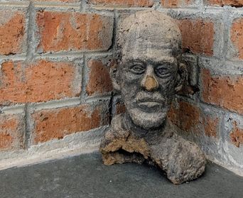 A rough clay bust of a bearded man’s head, displayed in the corner of a brick-walled room at Kara.