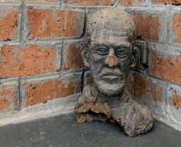 A rough clay bust of a bearded man's head, displayed in the corner of a brick-walled room at Kara.