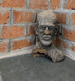 A rough clay bust of a bearded man's head, displayed in the corner of a brick-walled room at Kara.