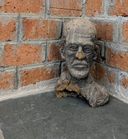 A rough clay bust of a bearded man’s head, displayed in the corner of a brick-walled room at Kara.