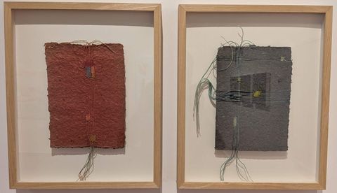 Two framed pieces of textured handmade paper artwork stitched with coloured thread, hanging on a white gallery wall at Muziris Contemporary.