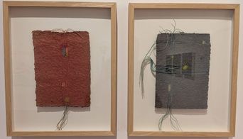 Two framed pieces of textured handmade paper artwork stitched with coloured thread, hanging on a white gallery wall at Muziris Contemporary.