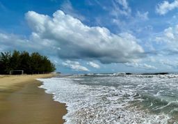 Empty sandy beach with a football goal frame near the tree line and breaking waves.