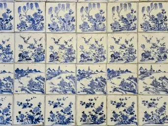 Rows of blue-and-white Chinese porcelain tiles, each hand-painted with a different floral or landscape scene, covering the synagogue floor.