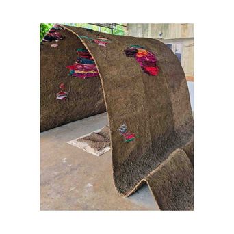 A large curved shelter built from dried mud and dung, standing on a concrete floor, with bundles of brightly coloured cloth pressed into its surface.