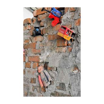 Broken plastic toys — a red lorry, a tractor, a doll's head and limbs — set into the crumbling brick and plaster of an old wall.