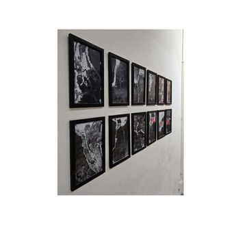 Twelve black-framed prints hung in two long rows on a white wall, each a close-up in stark black and white of a cracked, flaking surface.