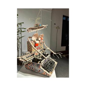 A tall figure built from an old typewriter and painted panels, with long jointed arms, a red bulb for a nose and a tangle of wire above its head.