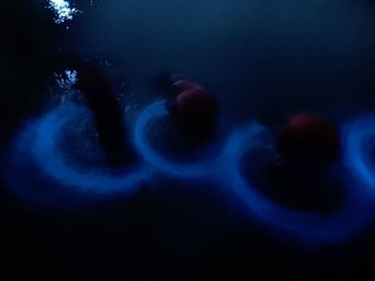 Three glowing blue rings spreading through dark water at night, where oars have dipped and stirred the surface.