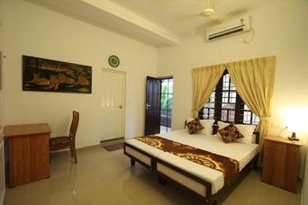 Bedroom with two single beds pushed together under a brown and gold runner, a painting of big cats on the wall, a wooden desk and an air conditioner high on the wall.
