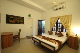 Bedroom with two single beds pushed together under a brown and gold runner, a painting of big cats on the wall, a wooden desk and an air conditioner high on the wall.