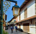 A yellow lantern and a Star of David sign hang over a narrow lane of white colonial buildings with wooden shutters near the synagogue.