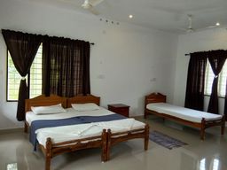 Bedroom with a wooden double bed and a single bed, both with white linen, dark brown curtains at tall windows, ceiling fans, a small wooden bedside table and a striped rug on a glossy floor.