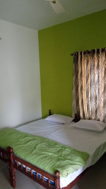 A bedroom with a double bed under a lime-green bedspread, a bright green wall behind it, and a wavy brown-and-cream curtain at the window.