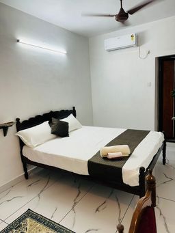 Bedroom with a dark wooden bed under white bedding and a dark runner, a wall-mounted air conditioner, and a marble-patterned tiled floor.