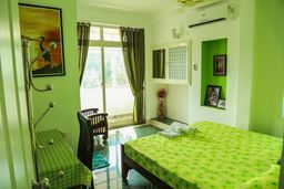 Bright green bedroom with a double bed under a green cover, a glass door with curtains onto a balcony, and a wall-mounted air conditioner.