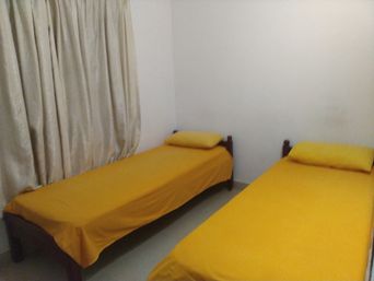 Small room with two single beds covered in yellow bedding, a cream curtain on the left wall and plain white walls.