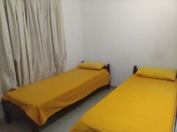 Small room with two single beds covered in yellow bedding, a cream curtain on the left wall and plain white walls.