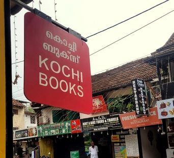 Red hanging signboard reading ‘Kochi Books’ above a street of shopfronts